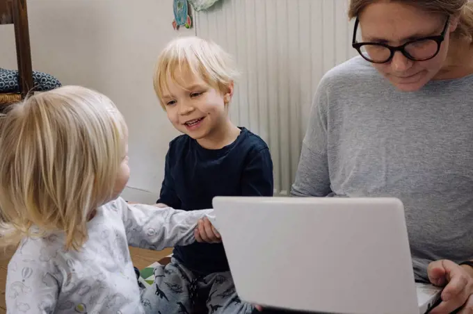 Mother with two little children working on laptop at home