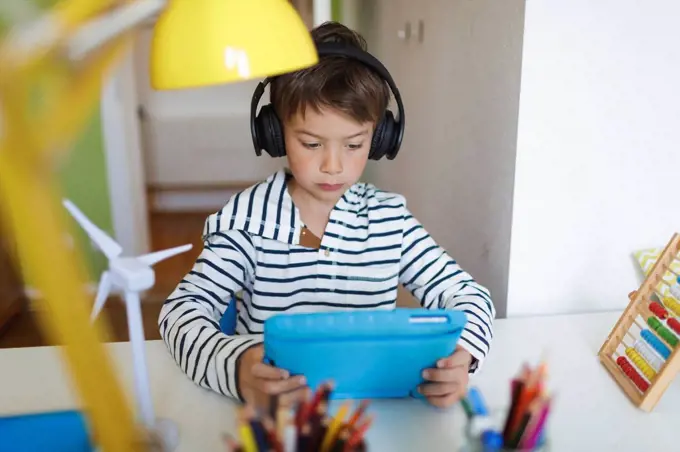 Boy doing homeschooling and using tablet and headphones at home
