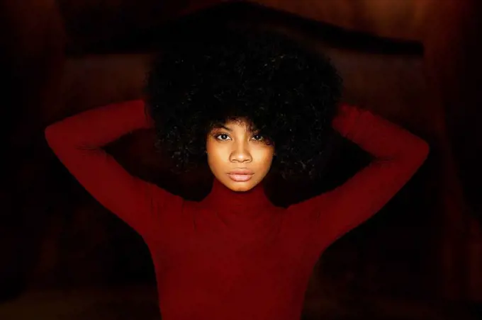 Portrait of young woman in red bodysuit, hands in hair