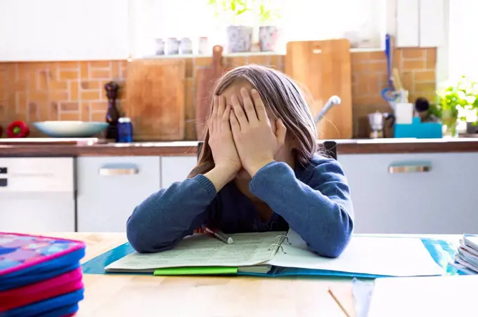 Girl doing homework in kitchen at home, hands on face