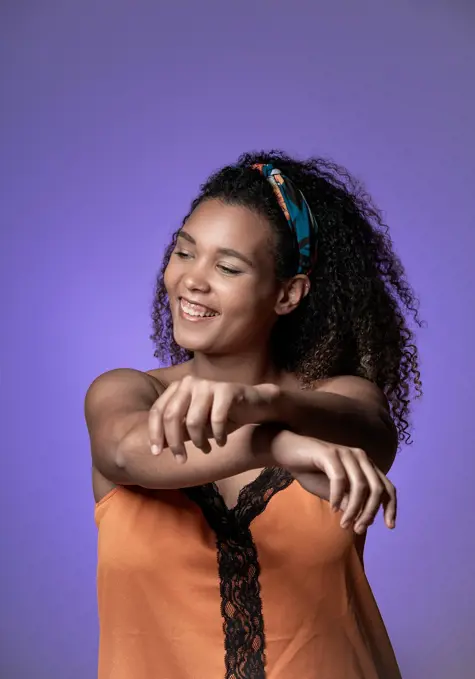 Cheerful young woman with curly hair dancing against purple background