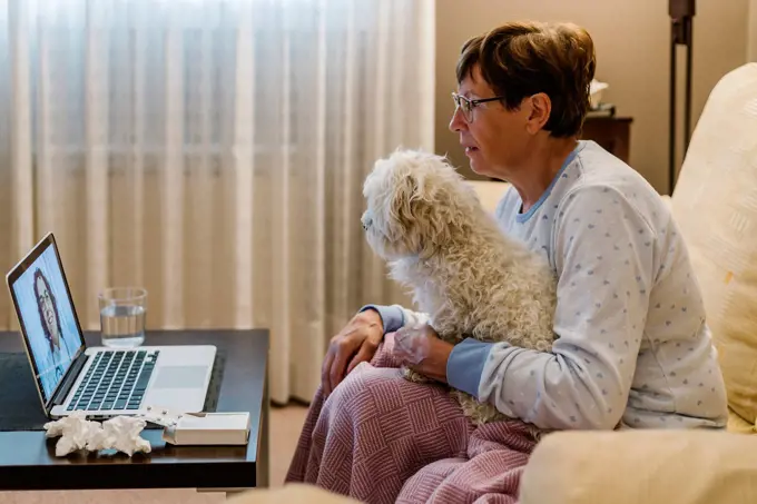 Ill senior woman discussing with doctor over video call while holding dog at home