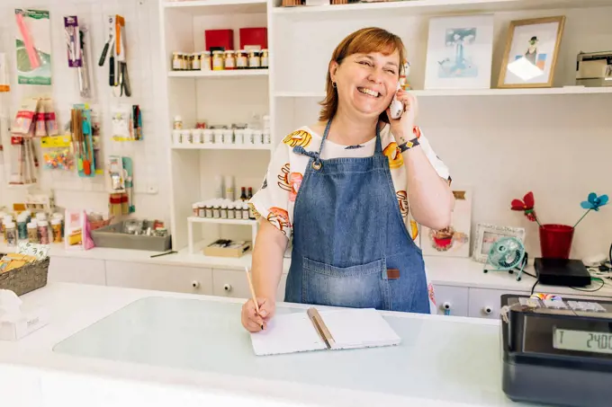 Smiling female baker taking order over phone in cake shop