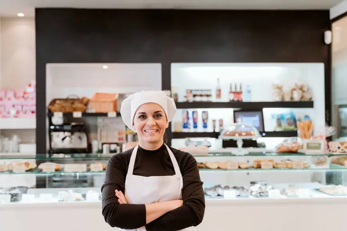 Happy female baker standing arms crossed at bakery