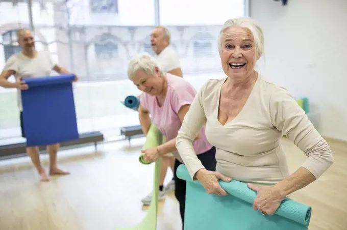 Laughing senior woman rolling up mat after yoga class
