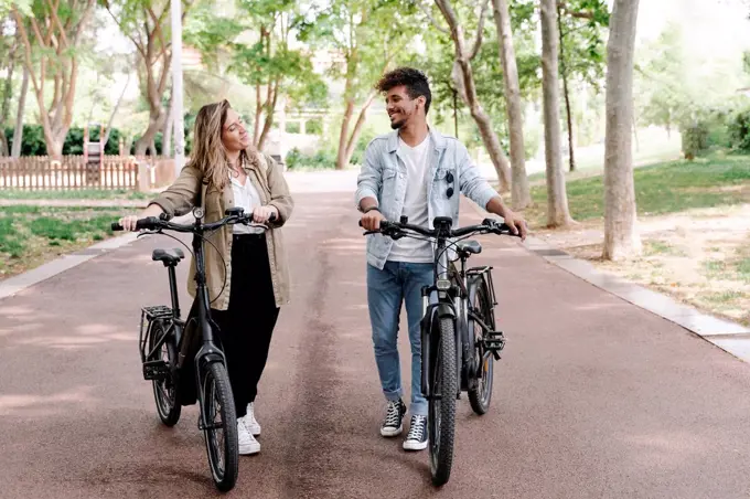 Smiling young couple with electric bicycles walking on road