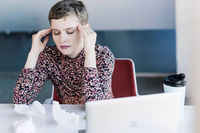 Businesswoman at desk in office having headaches