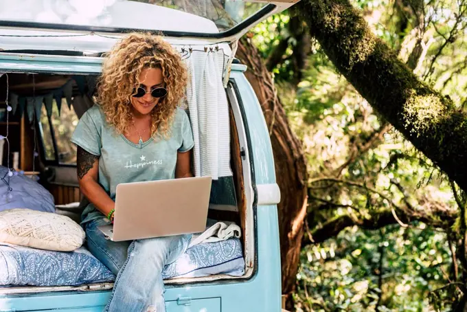 Woman wearing sunglasses using laptop while sitting on bed in vintage motor home