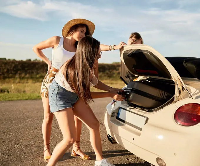 Female friends removing suitcase from car trunk