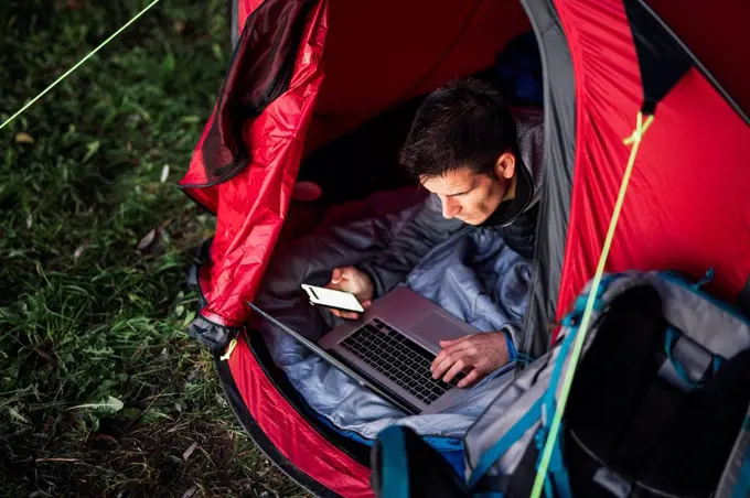 Man camping in Estonia, sitting in tent, using laptop
