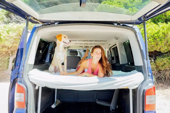 Woman with dog lying on bed in motor home at beach