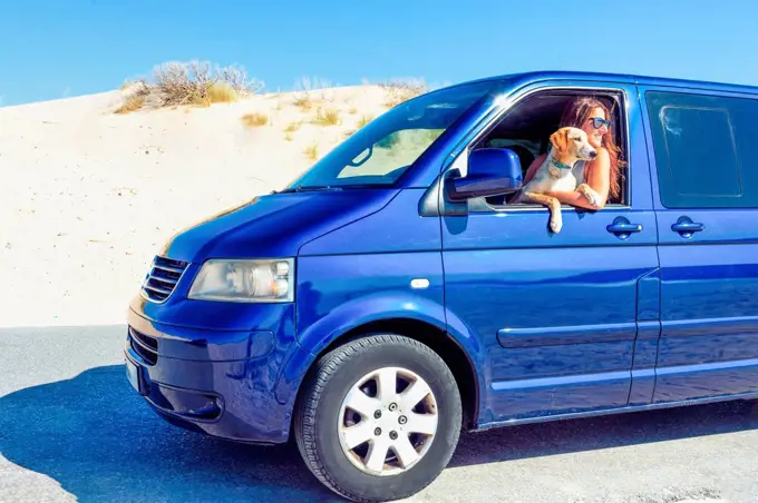 Woman with dog looking through window while sitting in blue motor home at beach