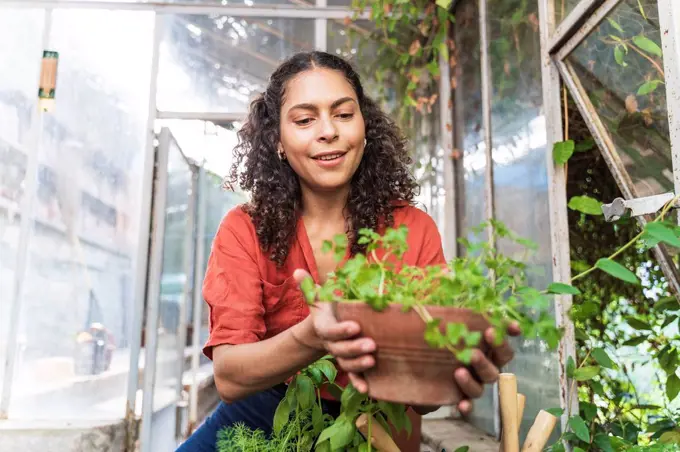Woman holding plant while sitting in garden shed
