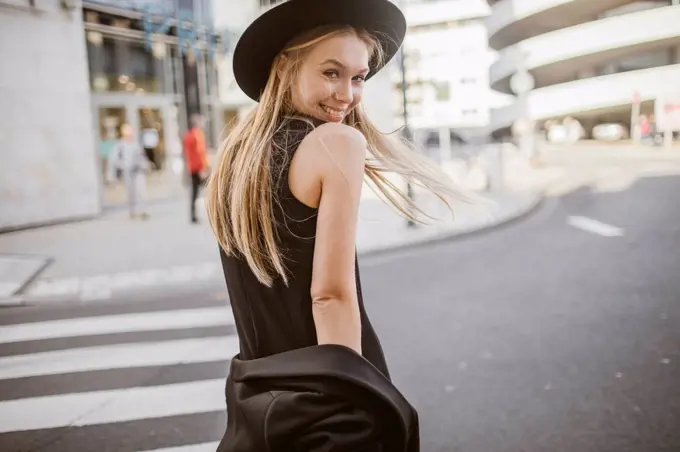 Smiling woman looking over shoulder while standing on street