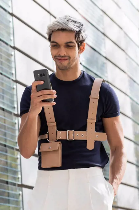 Smiling man with hand in pocket using smart phone in city