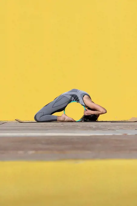 Woman doing yoga wheel exercise while bending over backwards by wall