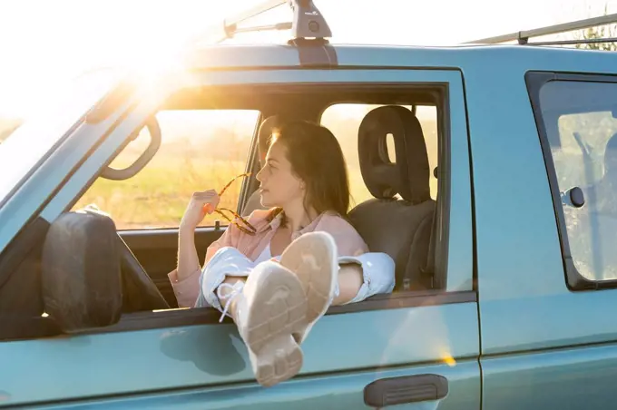 Young woman looking away while sitting with feet up on car window during road trip