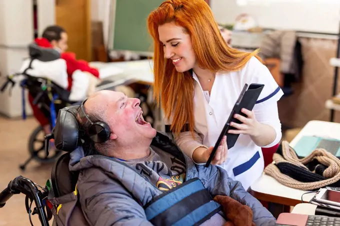 Smiling nurse showing digital tablet to happy disabled man in nursing home
