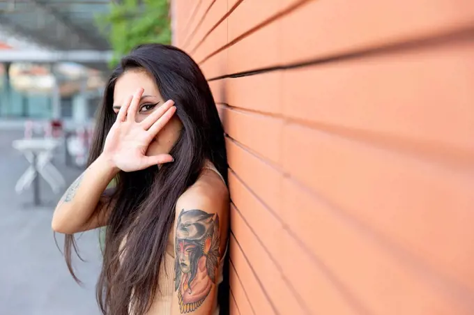 Woman looking through finger while leaning on wall