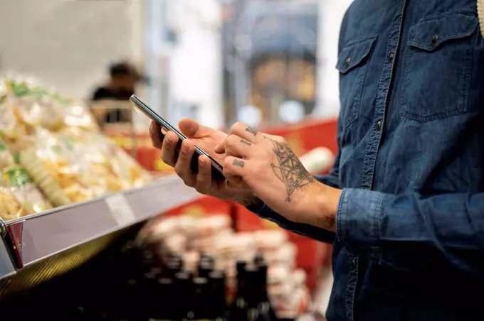 Close-up of mid adult man using smart phone in supermarket