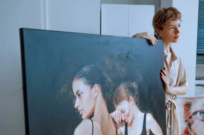 Thoughtful female artist standing by painting in art studio