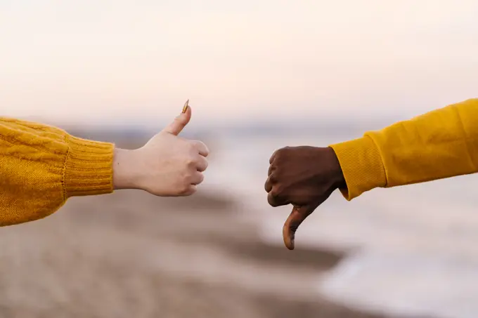 Woman and man showing thumps up and down gesture at beach