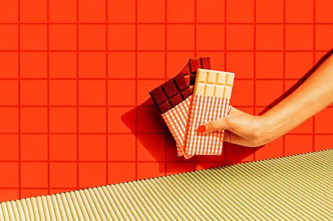 Female hand holding chocolate bars against red tile wall