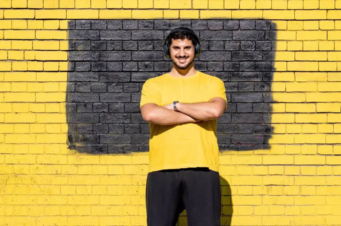 Smiling man with headphones standing against yellow brick wall