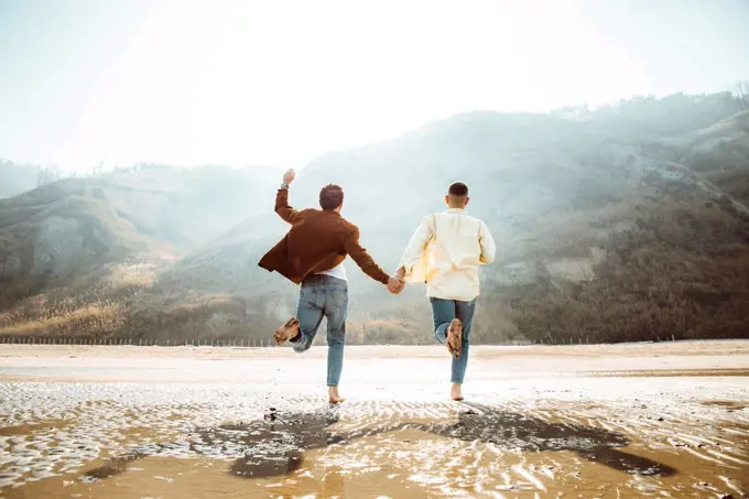 Homosexual couple holding hands and running at beach