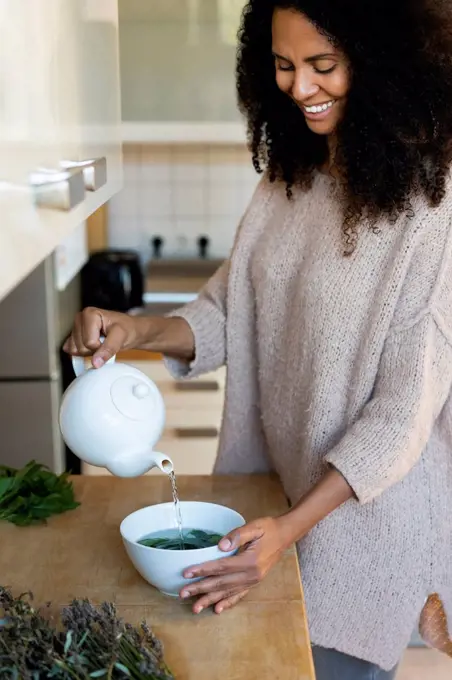 Happy woman pouring water in bowl while to prepare tea at home