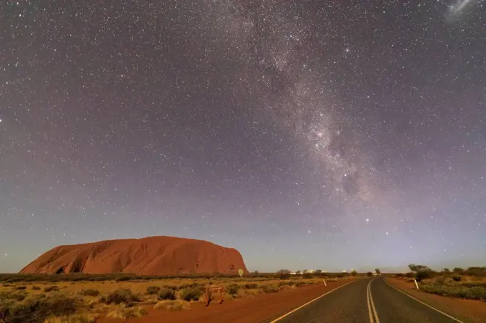 Australia, Northern Territory, Milky Way galaxy over Uluru (Ayers Rock) and empty highway at dusk
