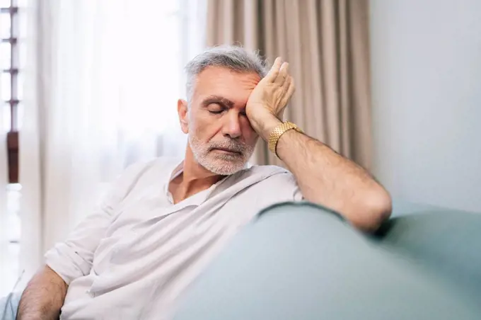 Tired man rubbing eyes while sitting on sofa in hotel room