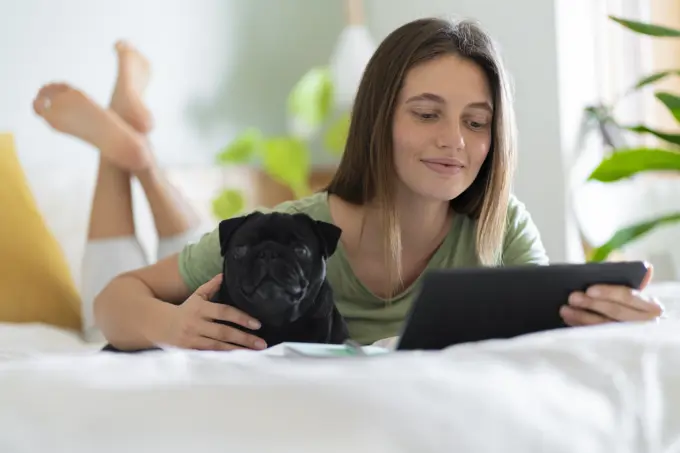 Young woman embracing Pug dog while using digital tablet at home