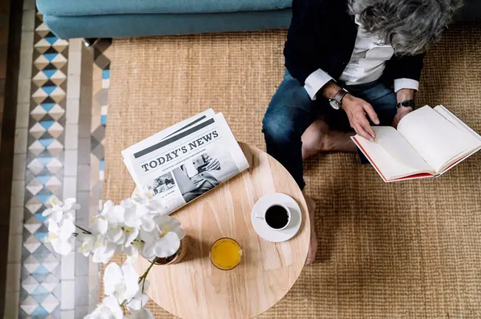 Man reading book while coffee and juice by newspaper on wooden table at home