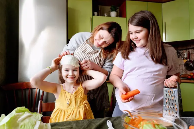 Playful mother and smiling daughters preparing food in kitchen at home