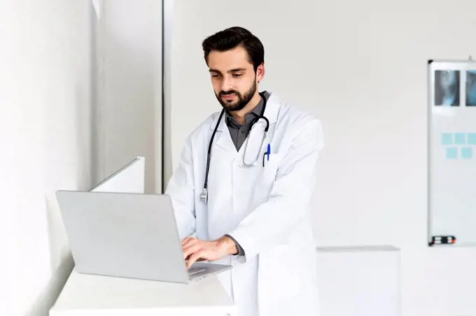Handsome male doctor using laptop in hospital