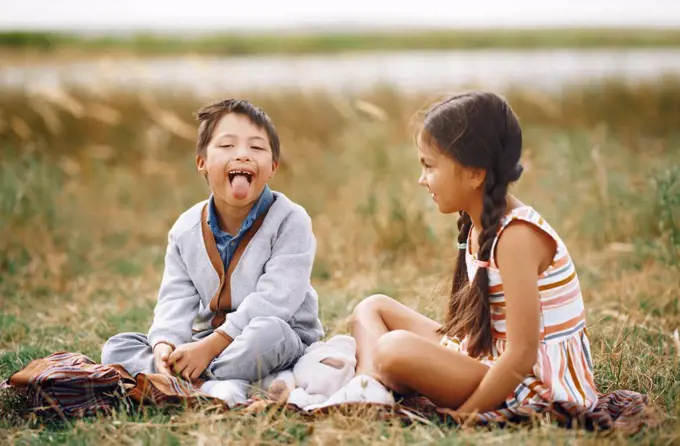Girl looking at brother with down syndrome sticking out tongue while sitting on grass