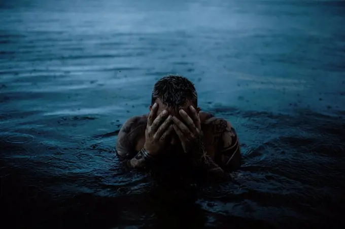 Man touching face in sea in rain