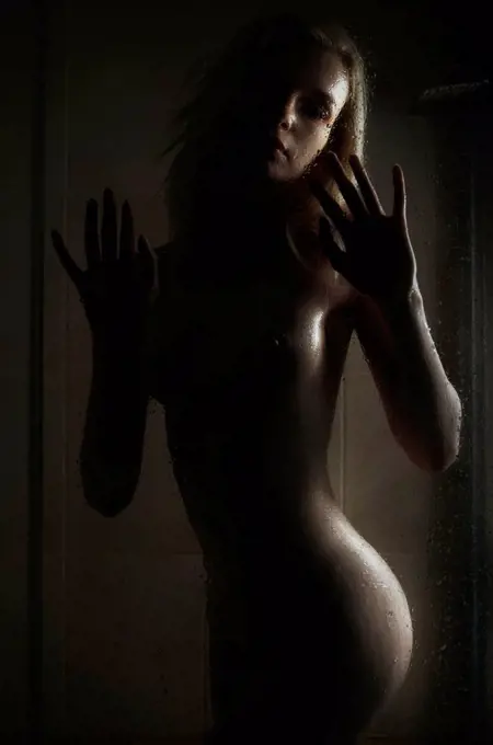 Naked young woman behind glass in bathroom