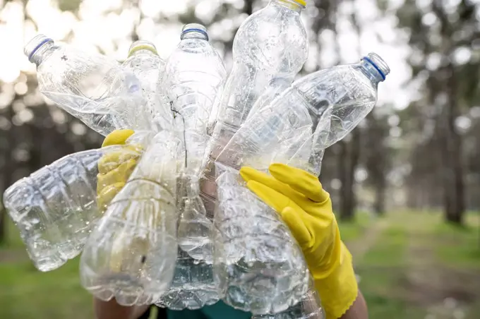 Volunteer holding crumpled plastic bottles in forest