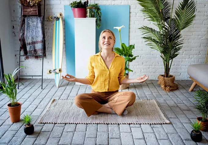 Young woman meditating while sitting on mat at home