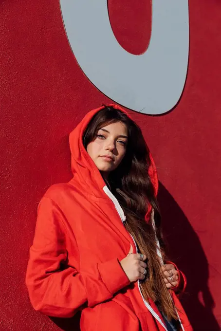 Teenage girl wearing red jacket while leaning on wall