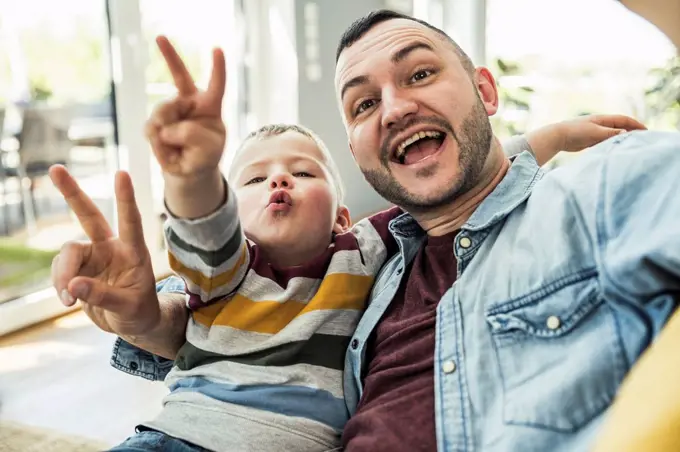 Happy father and son gesturing peace sign in living room at home