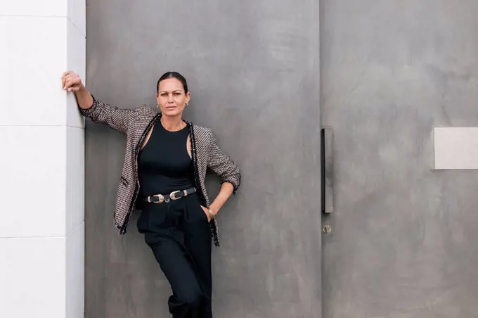 Businesswoman wearing jacket leaning on gray wall