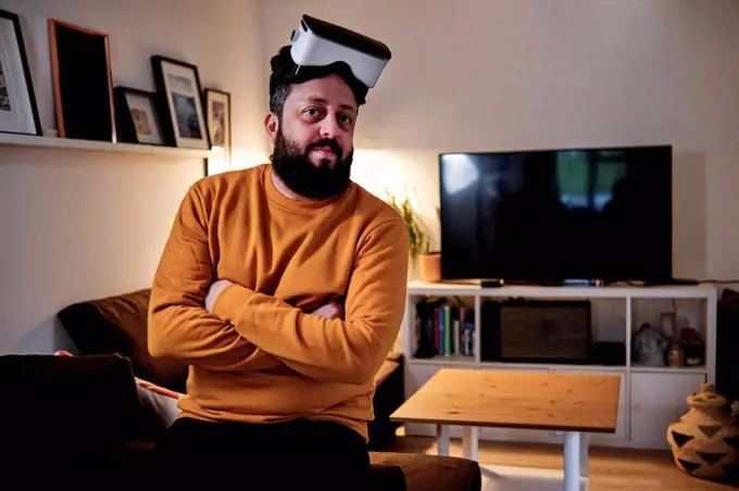 Mature man with arms crossed wearing virtual reality simulator at home