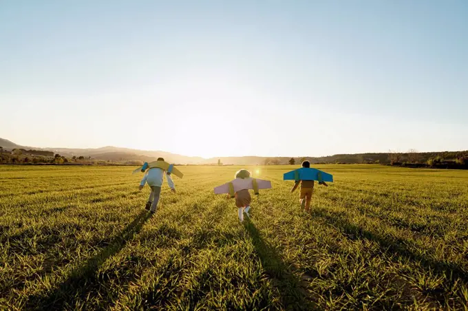 Playful brothers and sister with rocket wings running on agricultural field during sunny day