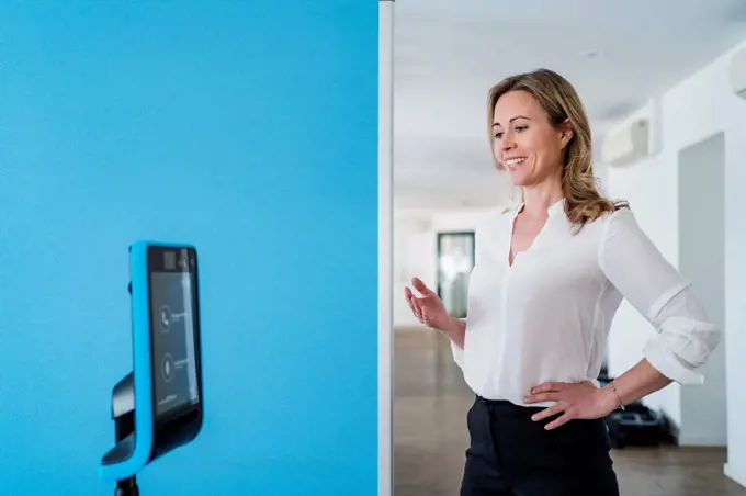 Businesswoman with hand on hip gesturing in front of assistant robot at office
