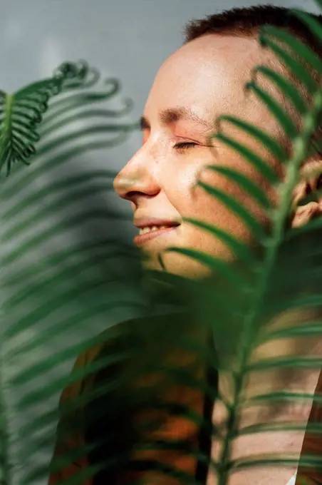 Smiling female entrepreneur with eyes closed by green leaves