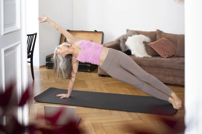 Mature woman wearing sports clothing practicing yoga at home