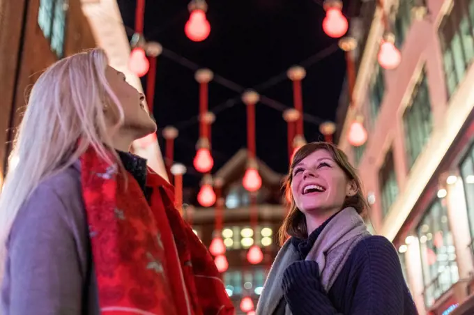Smiling female friends looking up at Christmas lights during holiday